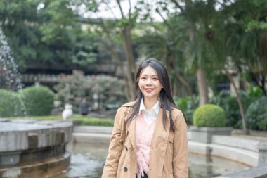 20 'li yaşlarında uzun saçlı Tayvanlı bir kadın, 30 Ocak 2024' te Tayvan 'ın Taipei kentindeki Xinyi İlçesi' ndeki bir parkta kış öğleden sonrasını bej renkli bir trençkot giyerek geçirir..