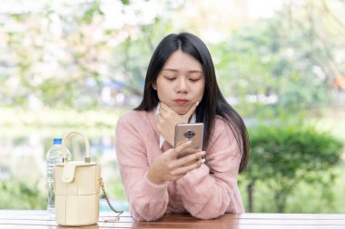30 Ocak 2024 'te Tayvan' ın Tayvan şehrinde Xinyi İlçesi 'nde bir bankta otururken 20' li yaşlarda pembe kazak giyen uzun saçlı bir Tayvanlı kadın akıllı telefon kullanıyor..