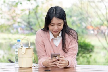 30 Ocak 2024 'te Tayvan' ın Tayvan şehrinde Xinyi İlçesi 'nde bir bankta otururken 20' li yaşlarda pembe kazak giyen uzun saçlı bir Tayvanlı kadın akıllı telefon kullanıyor..
