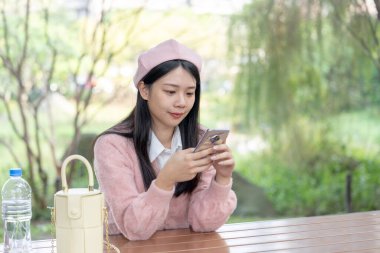 30 Ocak 2024 'te Tayvan' ın Tayvan şehrinde Xinyi İlçesi 'nde bir bankta otururken 20' li yaşlarda pembe kazak giyen uzun saçlı bir Tayvanlı kadın akıllı telefon kullanıyor..