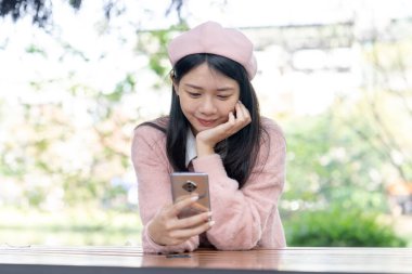 30 Ocak 2024 'te Tayvan' ın Tayvan şehrinde Xinyi İlçesi 'nde bir bankta otururken 20' li yaşlarda pembe kazak giyen uzun saçlı bir Tayvanlı kadın akıllı telefon kullanıyor..