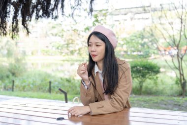 Tayvan 'ın Xinyi İlçesi' ndeki bir bankta oturan, 20 'li yaşlarda kahverengi trençkot giyen, uzun saçlı Tayvanlı bir kadın 30 Ocak 2024' te öğleyin çikolata yer..