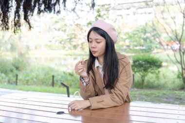 Tayvan 'ın Xinyi İlçesi' ndeki bir bankta oturan, 20 'li yaşlarda kahverengi trençkot giyen, uzun saçlı Tayvanlı bir kadın 30 Ocak 2024' te öğleyin çikolata yer..