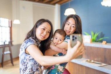 Two Taiwanese women in their 30s wearing traditional Chinese clothing hold a 6-month-old baby while taking a commemorative photo on Dihua Street in Taipei City, Taiwan, in September. clipart