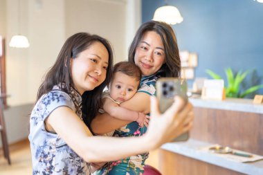 Two Taiwanese women in their 30s wearing traditional Chinese clothing hold a 6-month-old baby while taking a commemorative photo on Dihua Street in Taipei City, Taiwan, in September. clipart