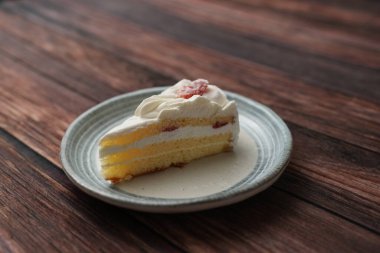 Kahverengi ahşap bir güvertede zarif bir Japon tabağında küçük bir Japon çilekli pasta..