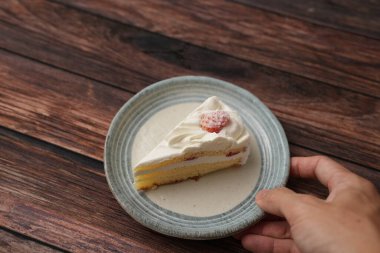 Sarı bir adamın eli, kahverengi ahşap bir güvertede Japon tarzı bir tabakta küçük bir Japon çilekli pasta yemek üzere..
