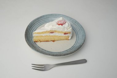 Küçük bir Japon çilekli pastası ve beyaz bir masada şık bir Japon tabağında küçük bir çatal..