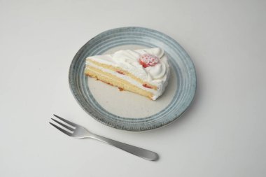 Küçük bir Japon çilekli pastası ve beyaz bir masada şık bir Japon tabağında küçük bir çatal..