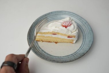 Küçük bir Japon çilekli pastası beyaz bir masada şık bir Japon tabağı ve yemek için küçük bir çatal tutan bir adam..