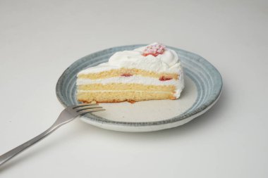 Küçük bir Japon çilekli pastası ve beyaz bir masada şık bir Japon tabağında küçük bir çatal..