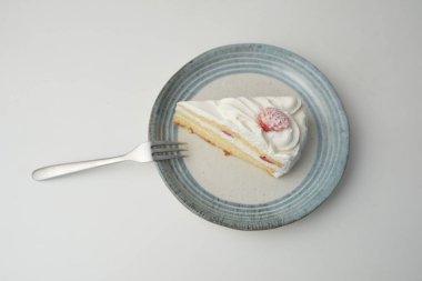 Küçük bir Japon çilekli pastası ve beyaz bir masada şık bir Japon tabağında küçük bir çatal..