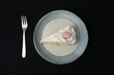 Küçük bir Japon çilekli pastası ve beyaz bir masada siyah bir bez üzerinde şık bir Japon tabağı üzerinde küçük bir çatal..