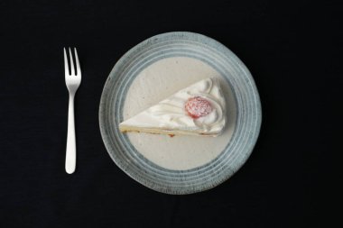 Küçük bir Japon çilekli pastası ve beyaz bir masada siyah bir bez üzerinde şık bir Japon tabağı üzerinde küçük bir çatal..