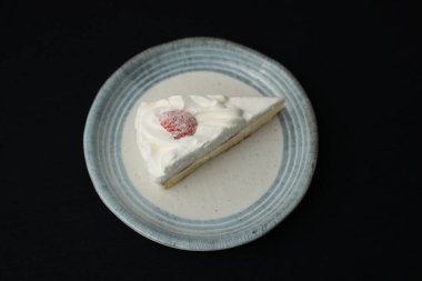 Küçük bir Japon çilekli pastası şık bir Japon tabağında beyaz bir masanın üstünde siyah bir bez üzerinde..