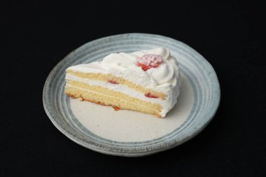 Küçük bir Japon çilekli pastası şık bir Japon tabağında beyaz bir masanın üstünde siyah bir bez üzerinde..