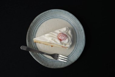 Küçük bir Japon çilekli pastası ve beyaz bir masada siyah bir bez üzerinde şık bir Japon tabağı üzerinde küçük bir çatal..