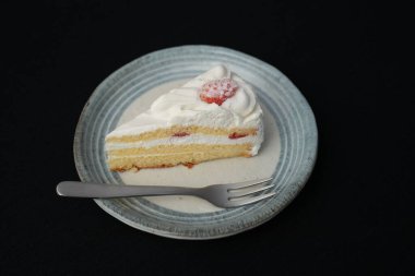 Küçük bir Japon çilekli pastası ve beyaz bir masada siyah bir bez üzerinde şık bir Japon tabağı üzerinde küçük bir çatal..