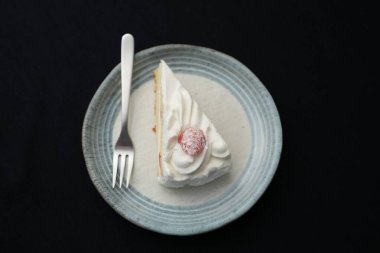 Küçük bir Japon çilekli pastası ve beyaz bir masada siyah bir bez üzerinde şık bir Japon tabağı üzerinde küçük bir çatal..