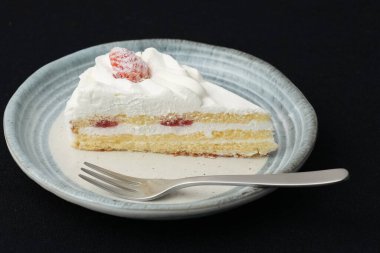 Küçük bir Japon çilekli pastası ve beyaz bir masada siyah bir bez üzerinde şık bir Japon tabağı üzerinde küçük bir çatal..