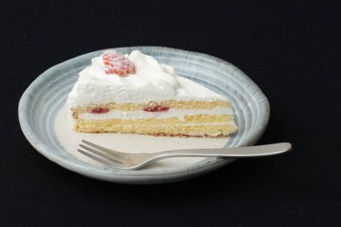 Küçük bir Japon çilekli pastası ve beyaz bir masada siyah bir bez üzerinde şık bir Japon tabağı üzerinde küçük bir çatal..