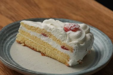 Küçük bir Japon çilekli pastası şık bir Japon tabağı üzerinde siyah bir bez üzerinde beyaz bir masa üzerinde ahşap bir tepside.