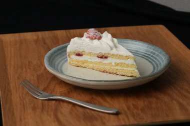 Küçük bir Japon çilekli pasta ve şık bir Japon tabağında küçük bir çatal beyaz bir masada siyah bir bez üzerinde ahşap bir tepside..