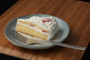 Küçük bir Japon çilekli pastası ve şık bir Japon tabağında büyük bir çatal beyaz bir masada siyah bir bez üzerinde ahşap bir tepside.