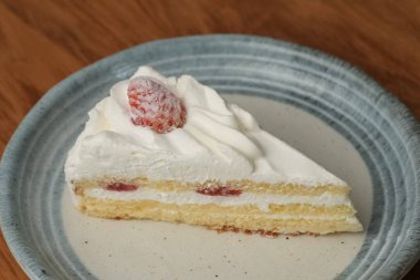 Küçük bir Japon çilekli pastası şık bir Japon tabağı üzerinde siyah bir bez üzerinde beyaz bir masa üzerinde ahşap bir tepside.