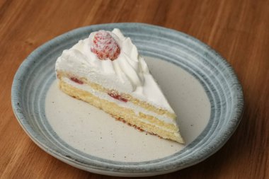 Küçük bir Japon çilekli pastası şık bir Japon tabağı üzerinde siyah bir bez üzerinde beyaz bir masa üzerinde ahşap bir tepside.