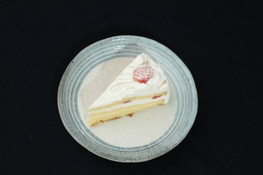 Küçük bir Japon çilekli pastası şık bir Japon tabağında beyaz bir masanın üstünde siyah bir bez üzerinde..