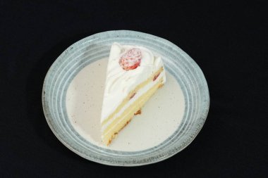 Küçük bir Japon çilekli pastası şık bir Japon tabağında beyaz bir masanın üstünde siyah bir bez üzerinde..