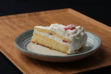 Küçük bir Japon çilekli pastası şık bir Japon tabağı üzerinde siyah bir bez üzerinde beyaz bir masa üzerinde ahşap bir tepside.