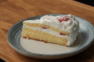 Küçük bir Japon çilekli pastası şık bir Japon tabağı üzerinde siyah bir bez üzerinde beyaz bir masa üzerinde ahşap bir tepside.