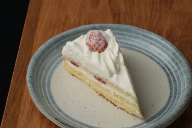 Küçük bir Japon çilekli pastası şık bir Japon tabağı üzerinde siyah bir bez üzerinde beyaz bir masa üzerinde ahşap bir tepside.