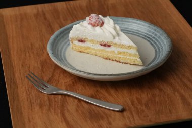 Küçük bir Japon çilekli pasta ve şık bir Japon tabağında küçük bir çatal beyaz bir masada siyah bir bez üzerinde ahşap bir tepside..