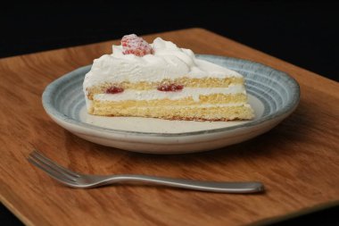 Küçük bir Japon çilekli pasta ve şık bir Japon tabağında küçük bir çatal beyaz bir masada siyah bir bez üzerinde ahşap bir tepside..