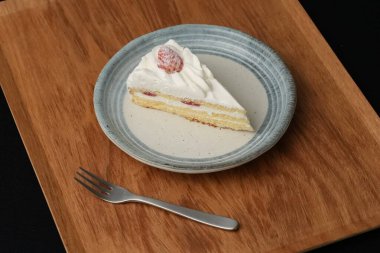 Küçük bir Japon çilekli pasta ve şık bir Japon tabağında küçük bir çatal beyaz bir masada siyah bir bez üzerinde ahşap bir tepside..