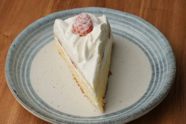 Küçük bir Japon çilekli pastası şık bir Japon tabağı üzerinde siyah bir bez üzerinde beyaz bir masa üzerinde ahşap bir tepside.