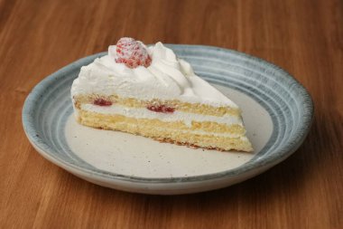 Küçük bir Japon çilekli pastası şık bir Japon tabağı üzerinde siyah bir bez üzerinde beyaz bir masa üzerinde ahşap bir tepside.