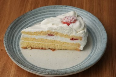 Küçük bir Japon çilekli pastası şık bir Japon tabağı üzerinde siyah bir bez üzerinde beyaz bir masa üzerinde ahşap bir tepside.