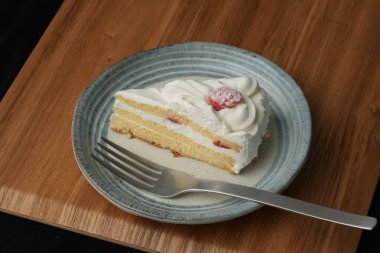 Küçük bir Japon çilekli pastası ve şık bir Japon tabağında büyük bir çatal beyaz bir masada siyah bir bez üzerinde ahşap bir tepside.