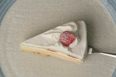 Beyaz bir masada Japon tarzı bir tabakta küçük bir Japon çilekli pasta ve onu kaldırmaya çalışan metal bir spatula..