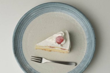 Küçük bir Japon çilekli pastası ve beyaz bir masada büyük bir çatal..