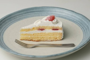 Küçük bir Japon çilekli pastası ve beyaz bir masada büyük bir çatal..