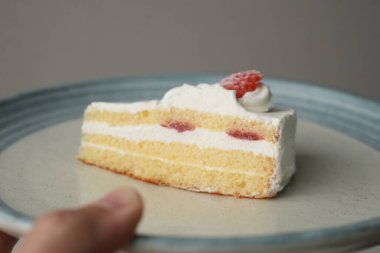 Japon eli küçük bir Japon çilekli pastasını beyaz bir masada büyük bir tabakta tutuyor..