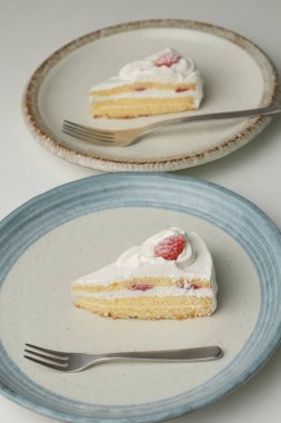 Japon çilekli pastası ve çatalı beyaz bir masadaki her şık büyük ve küçük tabakta..