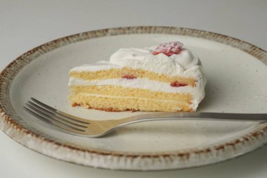 Küçük bir Japon çilekli pastası ve beyaz bir masada büyük bir çatal..