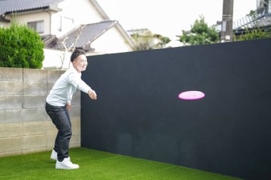 Japon bir ebeveyn ve çocuk, 20 'li yaşlarda bir adam ve 6 yaşında bir kız, evlerinin duvarlı bahçesinde bir öğleden sonra frizbi oynuyorlar..