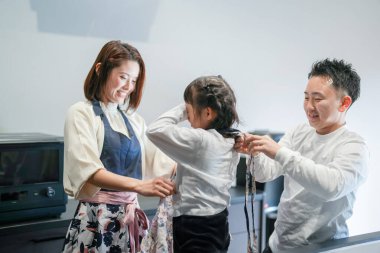 Japon bir ebeveyn ve çocuk, 30 'lu yaşlarda bir kadın, 20' li yaşlarda bir erkek ve 6 yaşında bir kız, evlerinin mutfağında önlük giyiyorlar..